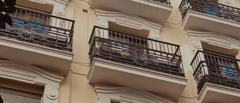 Un edificio de varios pisos con balcones, detalles arquitectónicos ornamentales y un cielo azul despejado.
