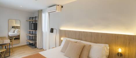 A modern hotel room with a large bed, a wooden headboard, a ceiling fan, a bedside table, and a mirror.
