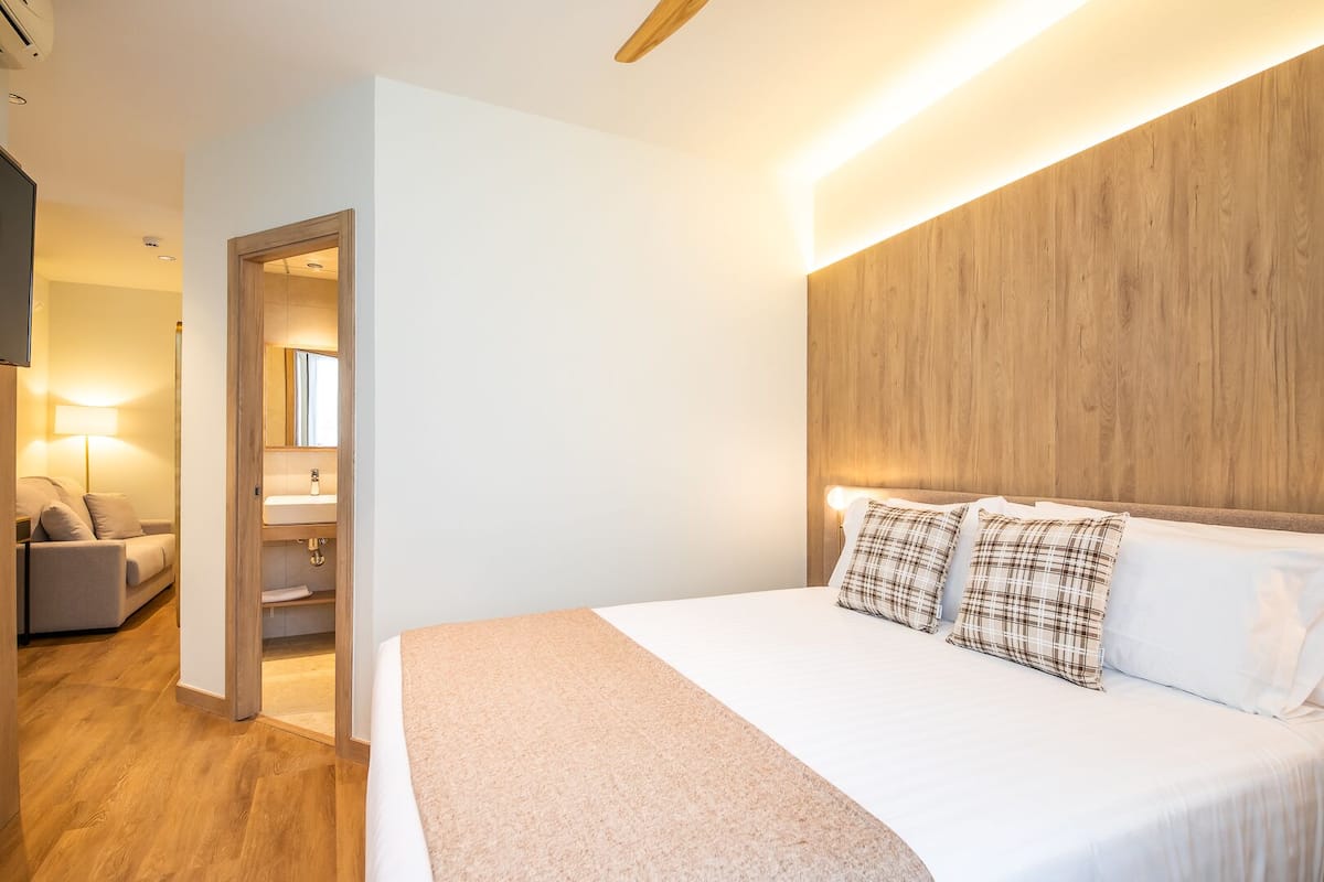 A modern hotel room with a large bed, a wooden headboard, a bedside table, and a lamp.