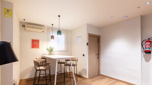 A modern kitchen with a white table, four bar stools, pendant lighting, and a fire extinguisher mounted on the wall. - Nommadas Jero Hotel - Adults Only (Valencia)