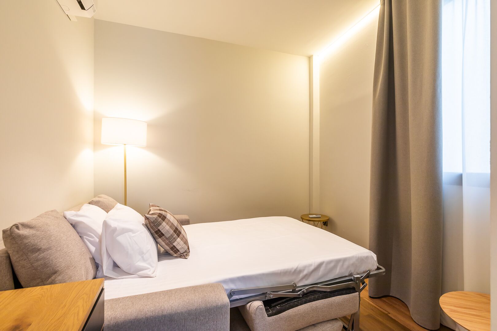 Habitación de hotel con cama, mesita de noche, lámpara y una pequeña mesa con control remoto.