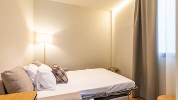 Habitación de hotel con cama, mesita de noche, lámpara y una pequeña mesa con control remoto.