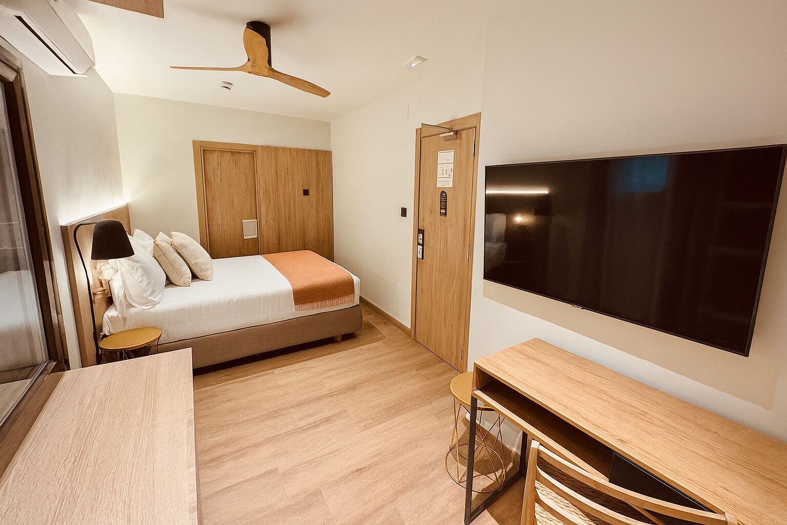 Una camera d'albergo moderna con un letto, una scrivania, una televisione e una ventola a soffitto.
