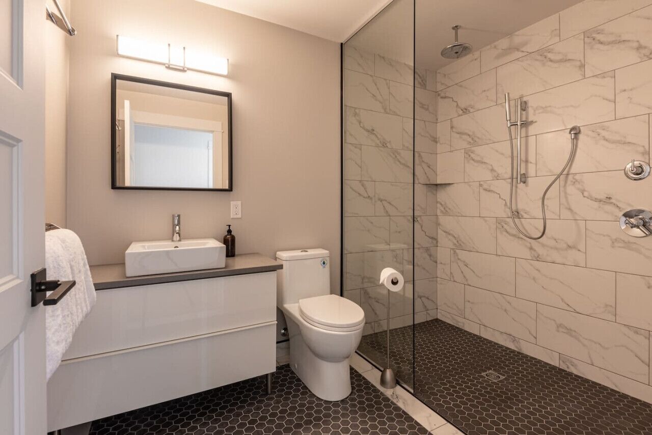 A modern bathroom with a glass-enclosed shower, a white toilet, and a vanity with a mirror and sink.