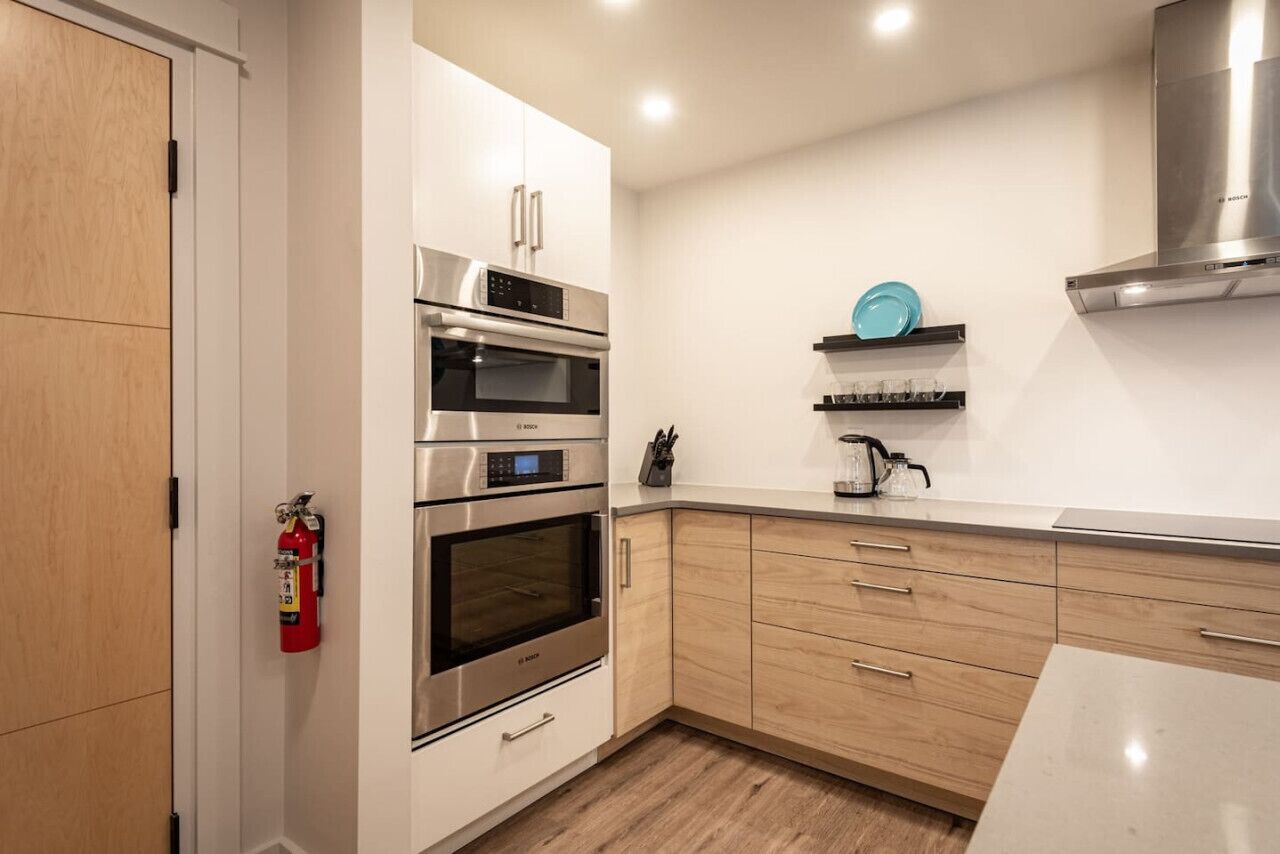 Una cocina moderna con electrodomésticos de acero inoxidable, armarios de madera y encimera blanca.
