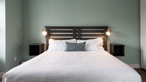 A bedroom with a large bed, two bedside tables, and a headboard with wall-mounted lights. - Suite 202- Two Bedroom apartment-style Suite w Balcony in Hybrid Hotel Wolfville (Wolfville)