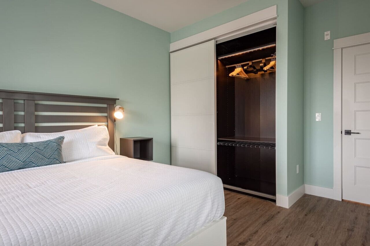 A bedroom with a bed, bedside table, and a walk-in closet with hanging clothes.