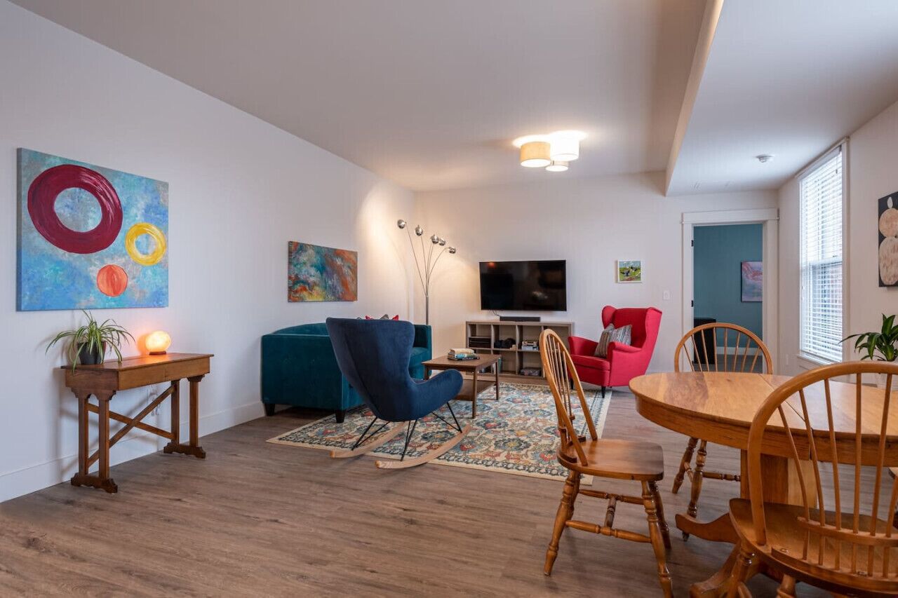 A modern living room with a blue sofa, a wooden dining table, and a TV.