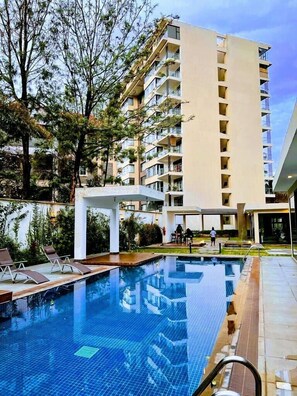 A swimming pool with lounge chairs, surrounded by a garden and a tall building with balconies. - Lux Suites Havana Luxurious Apartments (Nairobi)