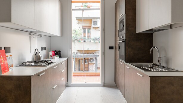 Une cuisine moderne dotée d’un îlot central, d’un four encastré et d’une grande fenêtre donnant sur un balcon.