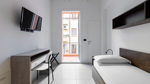 Une petite chambre moderne, équipée d’un lit, d’un bureau et d’un téléviseur fixé au mur.