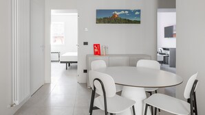 Une cuisine moderne avec des meubles blancs, une table à manger entourée de quatre chaises et un tableau représentant une montagne accroché au mur.