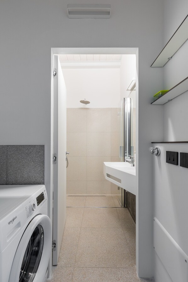 A modern bathroom with a washing machine, a shower, and a sink.