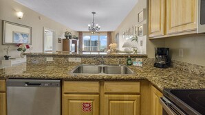 A kitchen with granite countertops, stainless steel appliances, wooden cabinets, and a view of the city through large windows. - Ariel Dunes II 803 *Beach views* 3 pools* (miramar beach)