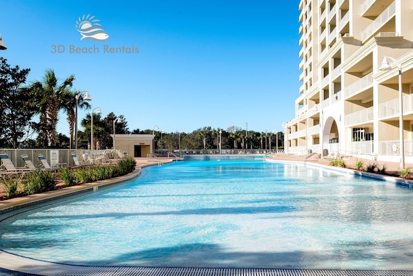 A swimming pool with lounge chairs, a small building, and a multi-story hotel with balconies.