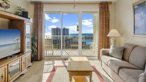 A living room with a television, a sofa, a table, and a balcony with a view of the ocean and buildings. - Ariel Dunes II 803 *Beach views* 3 pools* (miramar beach)