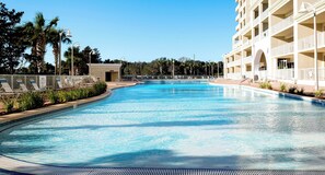 A large, clear swimming pool with lounge chairs and a building with multiple balconies in the background. - Ariel Dunes II 803 *Beach views* 3 pools* (miramar beach)