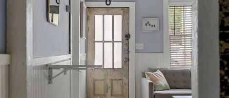 A hallway with a rustic wooden door, a cushioned bench, and a small table.