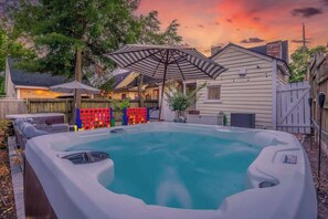 Un bain à remous dans un jardin, avec une clôture en bois, un patio couvert et des guirlandes lumineuses.