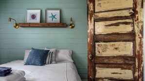 Une chambre à coucher avec un lit, des oreillers, une étagère en bois ornée de cadres photos et une porte rustique.