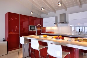 Una cocina moderna con armarios rojos, una isla central con taburetes y electrodomésticos de acero inoxidable, además de iluminación colgante.