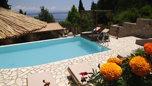 A swimming pool with stone tiles, a pergola, lounge chairs, and a view of the sea. - Corfu Dream Holidays Villas (Corfu)