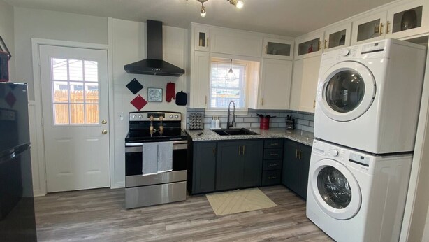 A modern kitchen with a built-in oven, a stove, a sink, and a stacked washer and dryer.