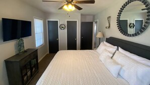 A bedroom with a bed, a ceiling fan, a TV, a dresser, and a mirror.
