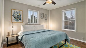 Ein Schlafzimmer mit einem Bett, einem Deckenventilator, einem Nachttisch und Kunstwerken an der Wand.
