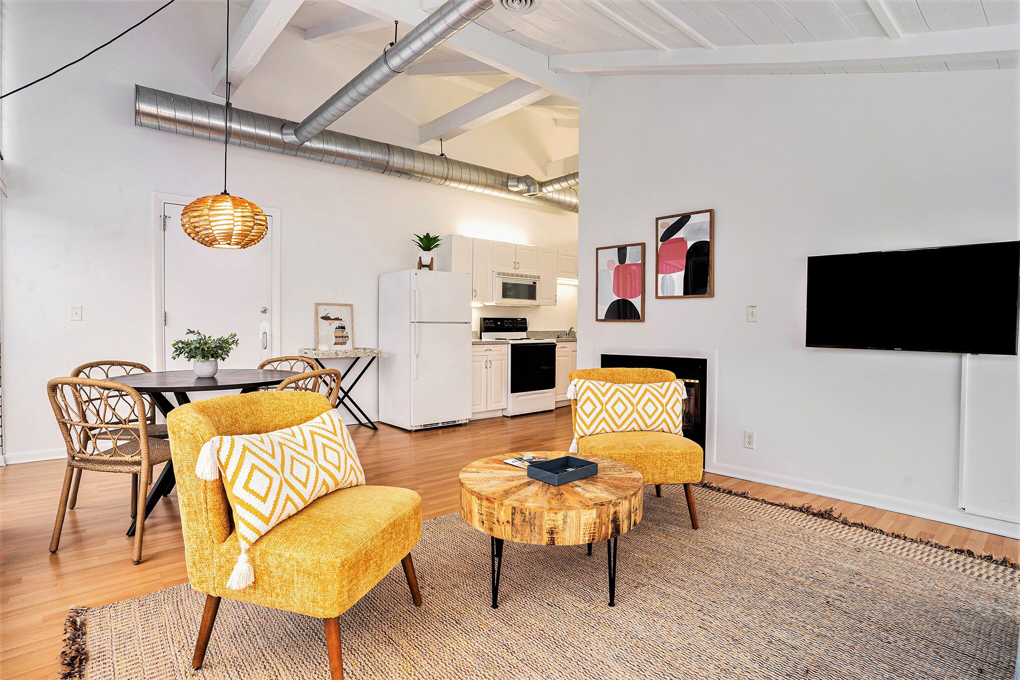 Uma sala de estar moderna com poltronas amarelas, uma mesa de centro redonda de madeira e uma TV de tela plana fixada na parede.