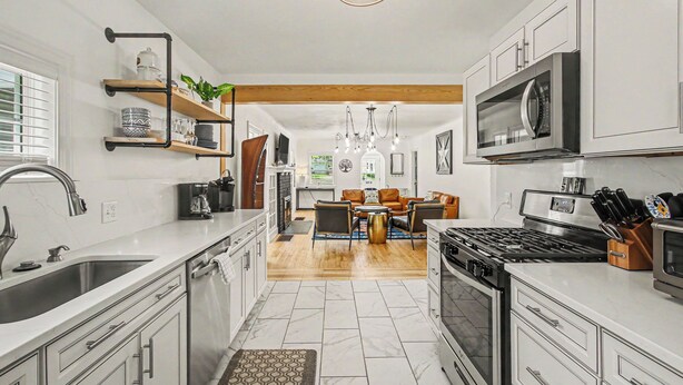 A modern kitchen with white cabinetry, a stainless steel sink, a built-in oven, and a microwave. There is a dining area with a wooden table and chairs, and a chandelier hanging above. - Retreat with hot tub, walking distance to town (Douglas)