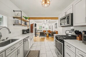 A modern kitchen with white cabinetry, a stainless steel sink, a built-in oven, and a microwave. There is a dining area with a wooden table and chairs, and a chandelier hanging above. - Retreat with hot tub, walking distance to town (Douglas)