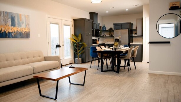 A modern living room with a sofa, a coffee table, and a dining area with chairs and a table.