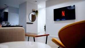 A modern living room with a wooden coffee table, a round mirror, and a flat-screen TV displaying the Netflix logo.