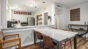 Una cocina moderna con una isla grande, luces colgantes y vistas al comedor.