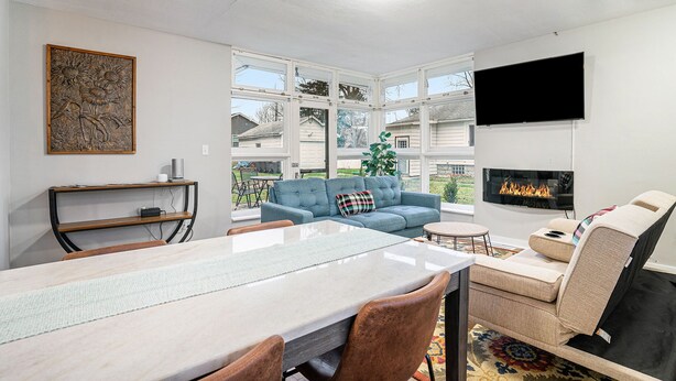 Sala de estar con mesa de comedor, sofá azul, chimenea, televisor y obras de arte en la pared.