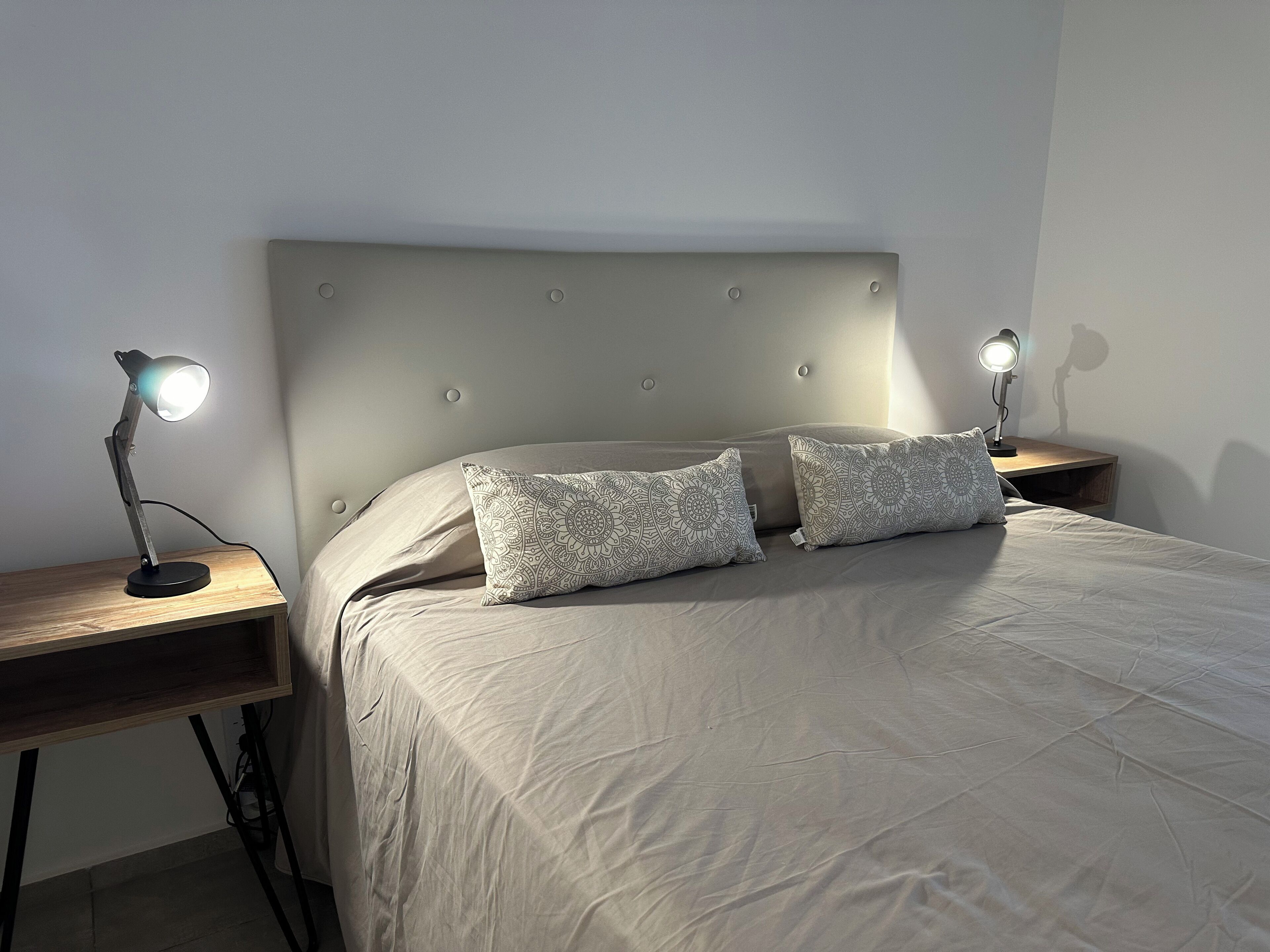 A neatly made bed with two patterned pillows, a headboard, and two bedside lamps on wooden nightstands.