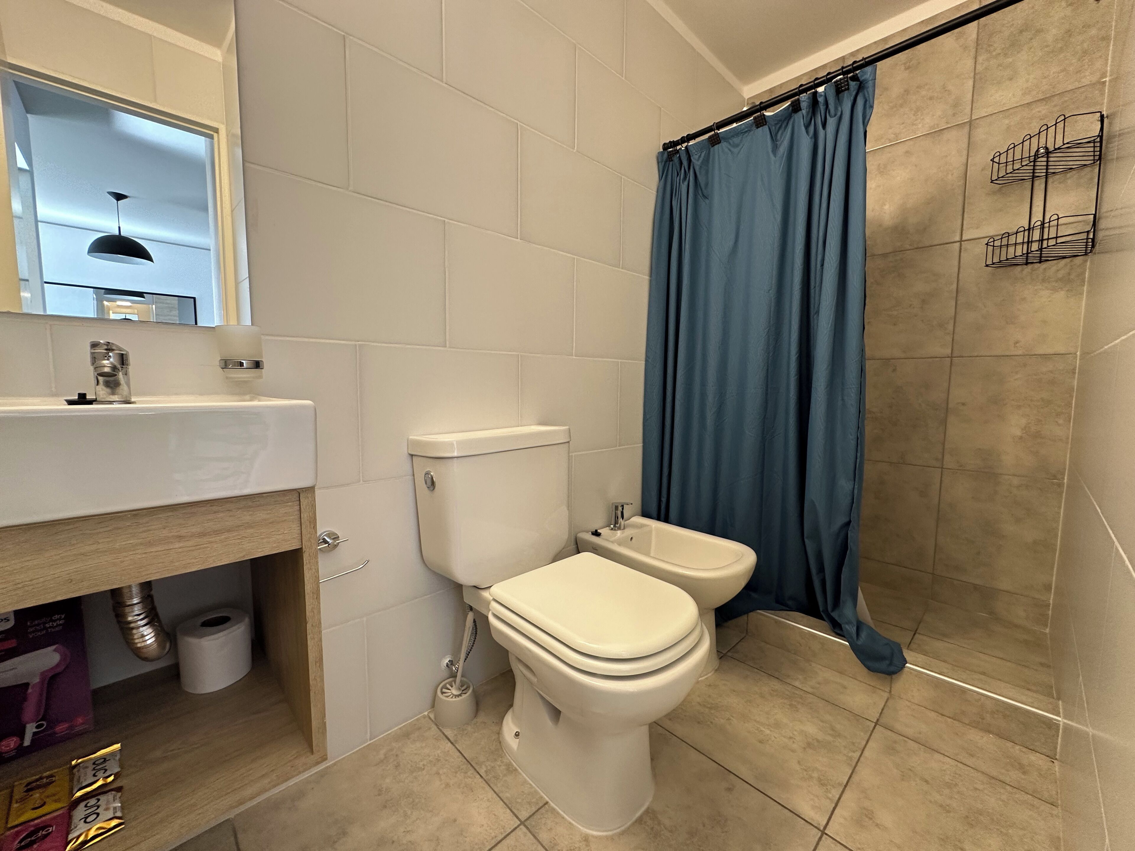 Baño con inodoro, bidé, lavabo y cortina de ducha.