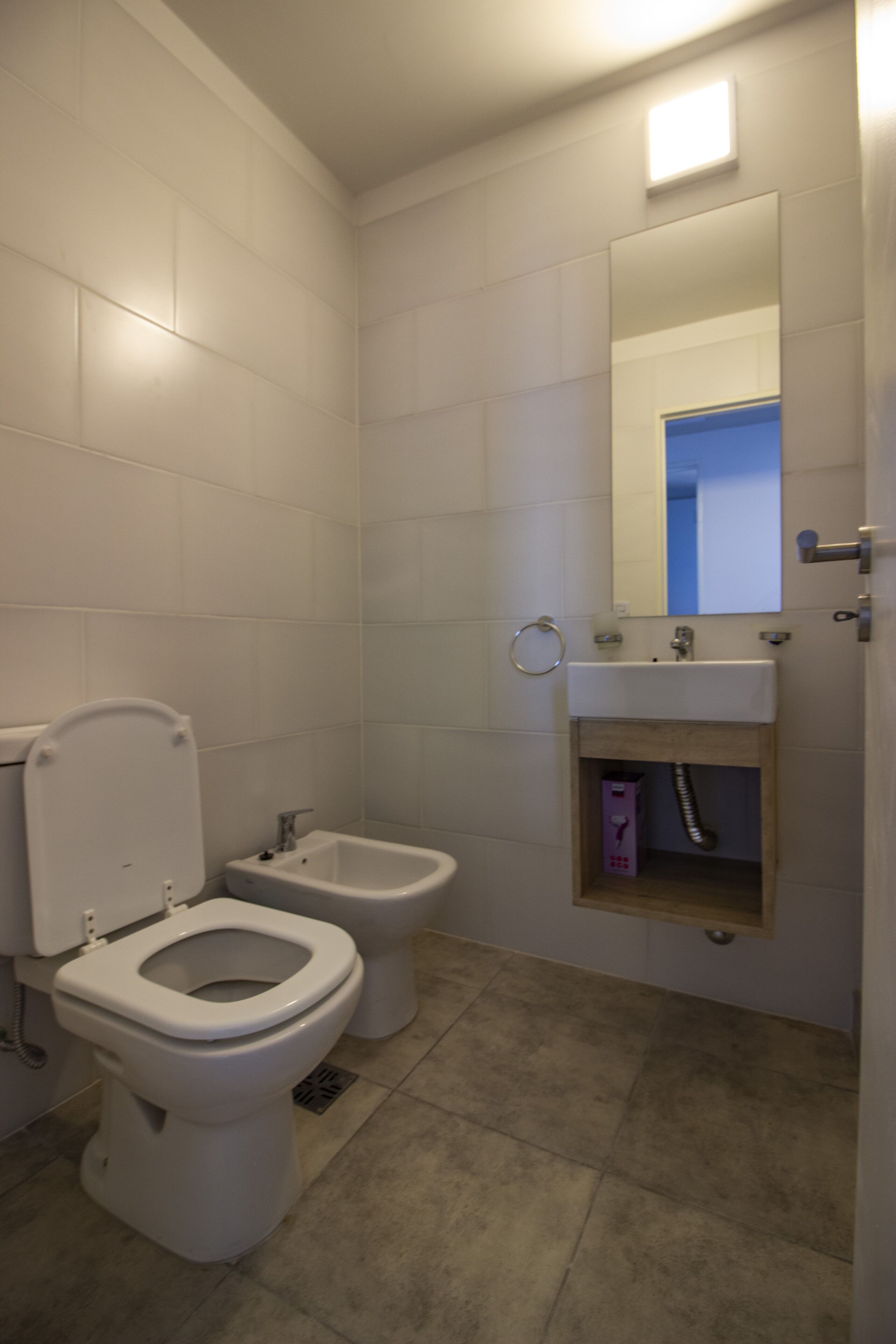 Un baño con inodoro, bidé, lavamanos y espejo.