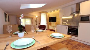 Una cocina moderna con comedor, que presenta una mesa de madera preparada para cuatro, una planta en maceta y un televisor de pantalla plana montado sobre la encimera.
