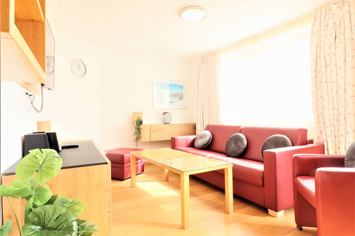 Ett modernt vardagsrum med en röd soffa, ett soffbord i glas och ett träskåp.
