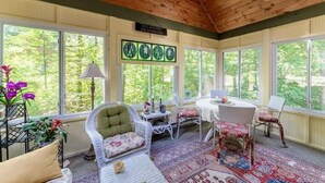 A sunroom with large windows, a wooden ceiling, and a table with chairs.