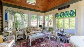 A sunroom with wicker furniture, a patterned rug, and a view of greenery outside.