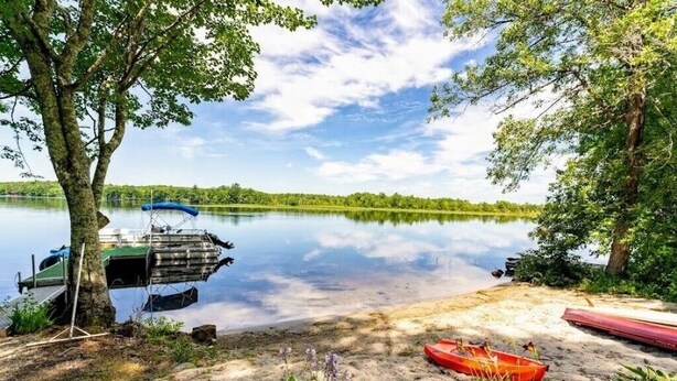 A calm lake with a dock, a red boat, and a green canopy.