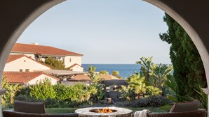 Eine Terrasse mit Korbmöbeln, einem Steinkamin und Blick aufs Meer.