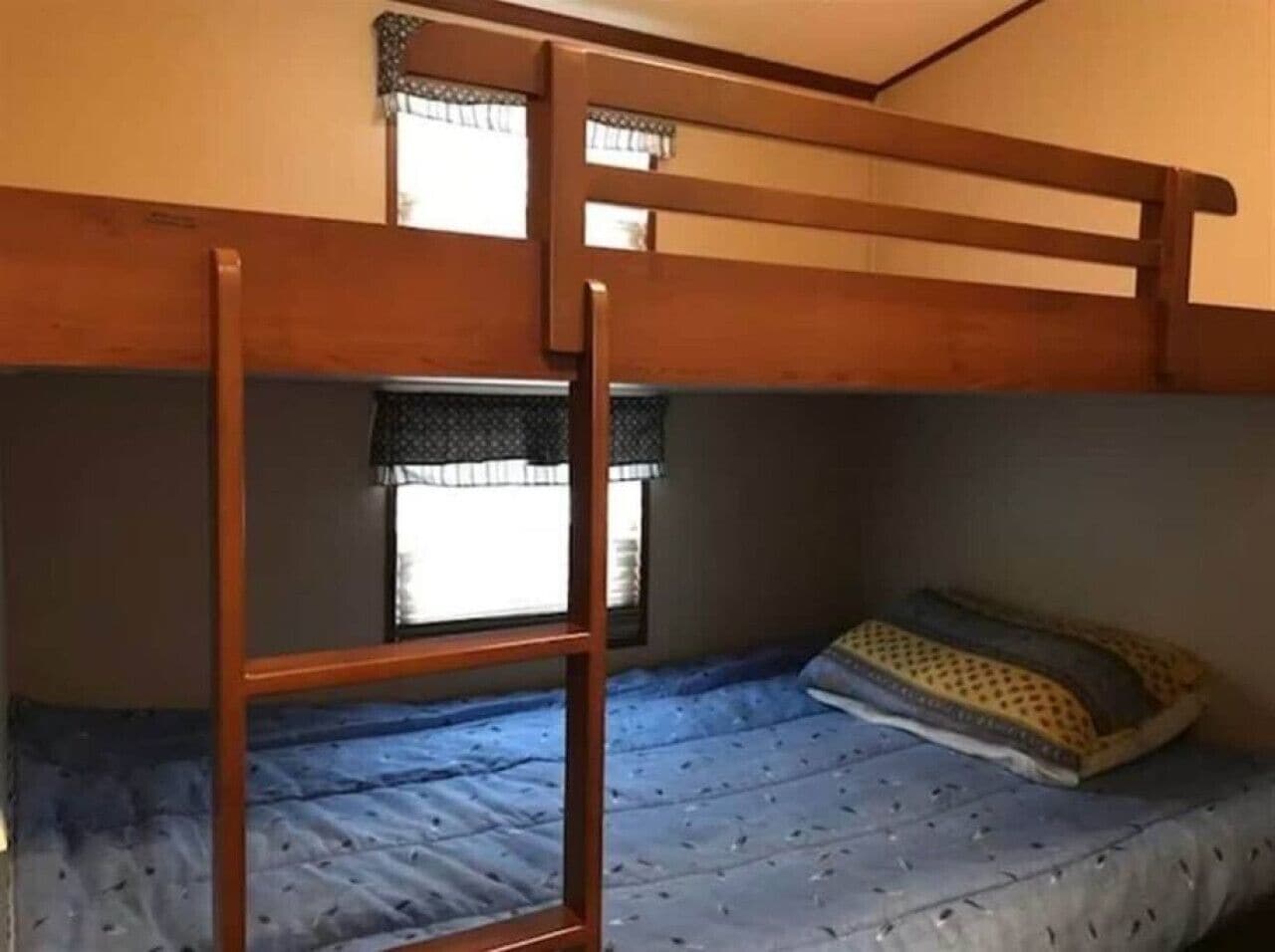Un lit superposé avec une échelle, une fenêtre ornée d’un rideau à motifs et un seul oreiller sur le lit du bas.