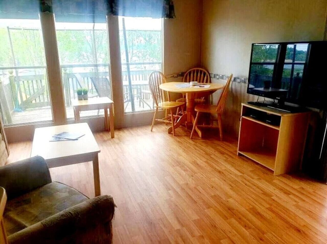 Ein Wohnzimmer mit Holzboden, einem Fernseher, einem Esstisch mit Stühlen und einem Balkon mit Geländer.