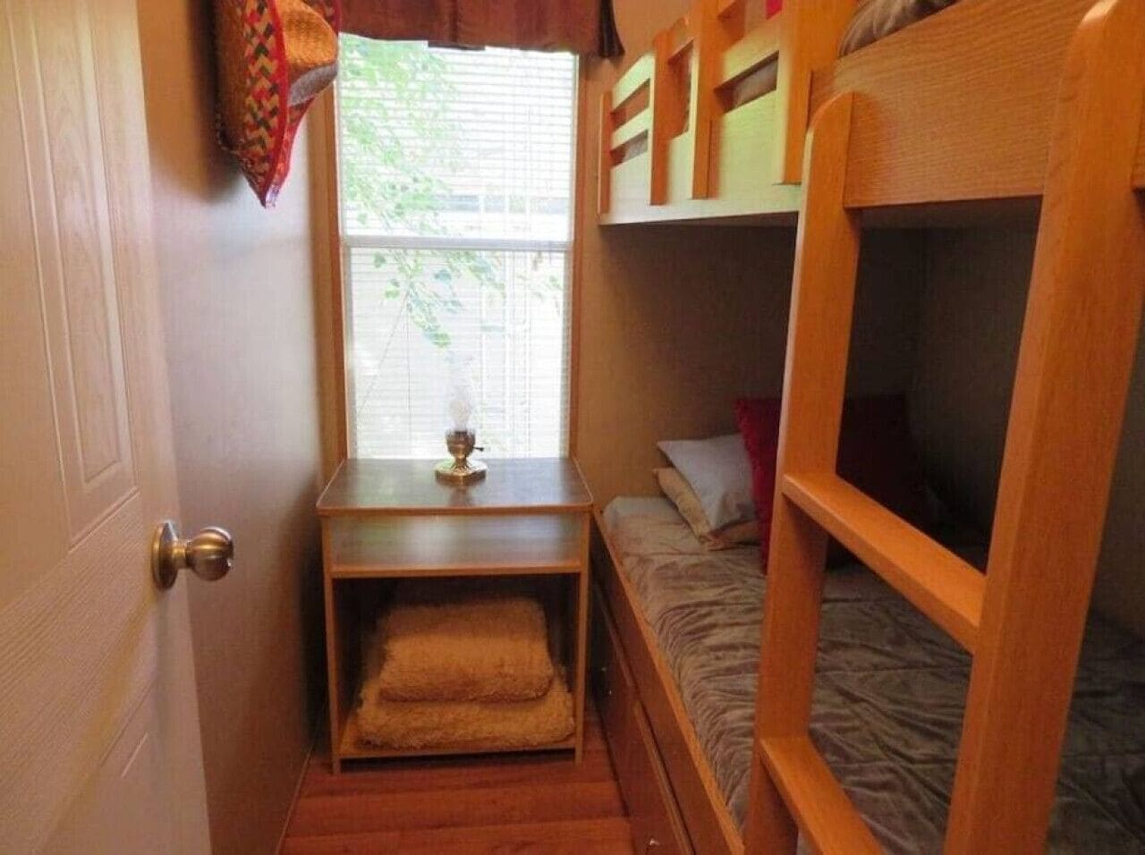 A compact room with bunk beds, a small table with a lamp, and a window with blinds.