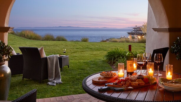 Un área de comedor al aire libre con vistas al mar, que incluye una mesa dispuesta con velas, copas de vino y una botella.