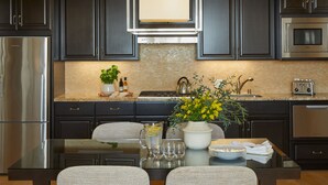 Una cocina moderna con armarios oscuros, electrodomésticos de acero inoxidable, una isla central con asientos y un jarrón decorativo con flores amarillas.